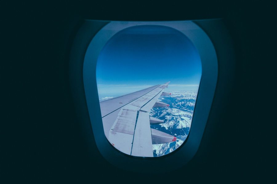 Aircraft wing over snowy mountains framed by an oval airplane window